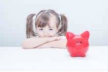 Child Girl Looks At A Red Piggy Bank Pig Standing On The Table