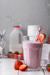 Wall Mural - Strawberry protein shake on a white wooden background. Fresh milkshake with strawberries on a light table. A glass of strawberry smoothie.