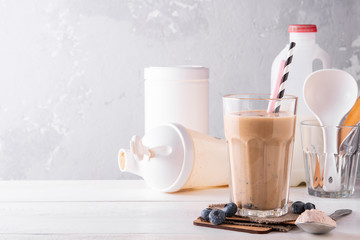 Wall Mural - Chocolate protein shake on a white wooden background. Fresh milkshake with blueberry on a light table. A glass of chocolate smoothie .