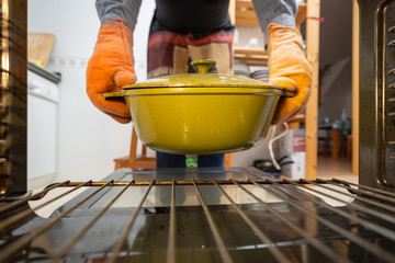 View from inside the oven of a person taking out a very hot enameled iron pot to roast chickens