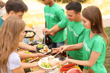 Wall Mural - Young volunteers giving food to poor people outdoors