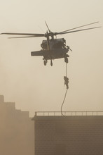 Military Combat And War With Helicopter Flying Into The Chaos And Destruction. Soliders Suspend From Rope To The Ground From Chopper. Military Concept Of Power, Force, Strength, Air Raid.
