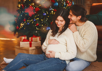 Wall Mural - Pregnant wife and her husband sitting by Christmas tree