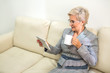© Alexandr - adult woman in a suit sitting on a sofa with a tablet and a cup in hand