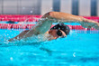 © Maridav - Swimmer man doing crawl swim in swimming pool portrait. Closeup of athlete wearing goggles, swimming cap training in blue water indoors.