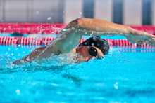 Swimmer Man Doing Crawl Swim In Swimming Pool Portrait. Closeup Of Athlete Wearing Goggles, Swimming Cap Training In Blue Water Indoors.