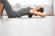 Girl doing yoga lying on massager on grey rug in gym