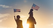 Leinwandbild Motiv Patriotic man, woman, and child waving American flags in the air. 