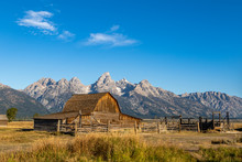 View Of An Old Wooden Barn At Sunrise With Mountains In The Background