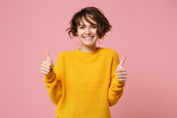 Wall Mural - Cheerful young brunette woman girl in yellow sweater posing isolated on pastel pink wall background, studio portrait. People sincere emotions lifestyle concept. Mock up copy space. Showing thumbs up.