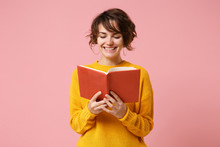 Smiling Young Brunette Woman Girl In Yellow Sweater Posing Isolated On Pink Wall Background, Studio Portrait. People Sincere Emotions Lifestyle Concept. Mock Up Copy Space. Holding And Reading Book.