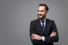 Smiling Young Business Man In Classic Black Suit Shirt Tie Posing Isolated On Grey Background. Achievement Career Wealth Business Concept. Mock Up Copy Space. Holding Hands Crossed, Looking Aside.