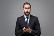 © ViDi Studio - Shocked young business man in classic black suit shirt tie posing isolated on grey background. Achievement career wealth business concept. Mock up copy space. Using mobile phone typing sms message.