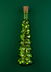 Wall Mural - Decorative bottle in the form of a Christmas tree on a green background.