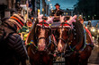 Horse wearing a hat with reindeer antlers and other Christmas decorations, haulin a cart decorated with christmas lights of multiple colors.