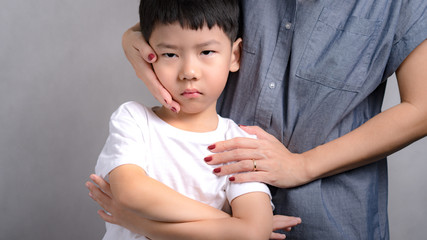 Portrait of adorable innocence little asian boy (3-6 years old) frown face expression feeling unhappy, disappointed while his Mom comforting, soothing him with love and care. Parenting child concept.