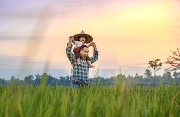 The son happily rode his father's neck and looked at the green fields at sunset.