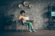 Full length photo of cool afro american girl college student sit table chair start work high-school presentation feel clever in office loft workstation wear yellow shirt green pants