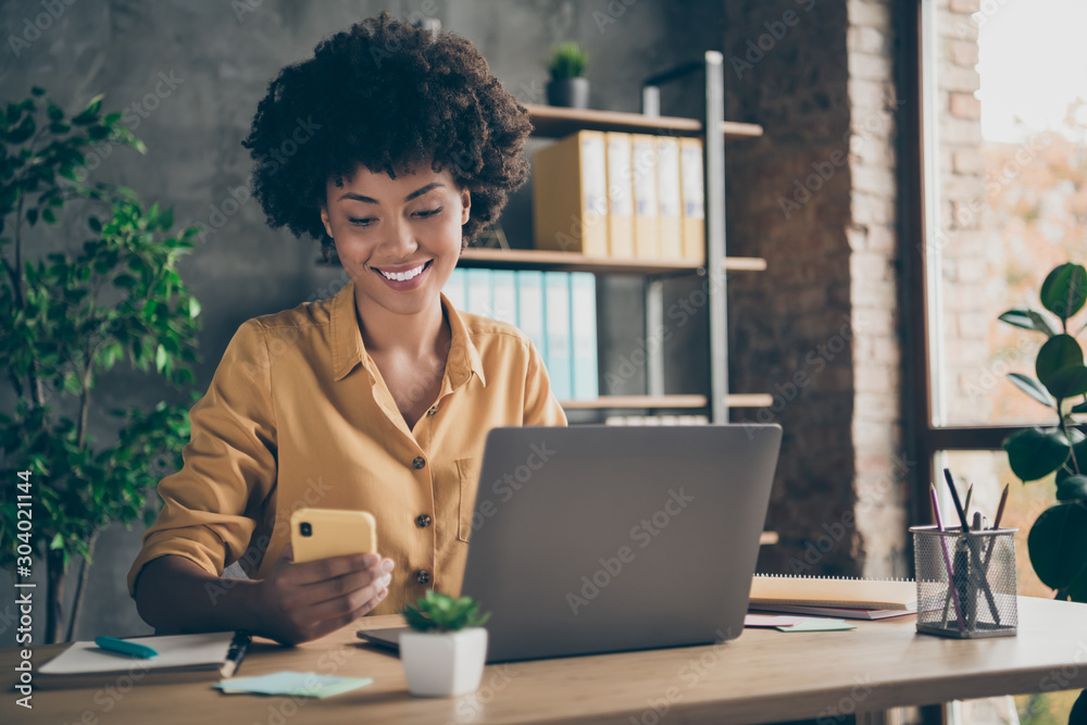 Photo of cheerful professional business lady in yellow shirt working as smm manager in a large international company browsing through telephone in search of appropriate content - obrazy, fototapety, plakaty 