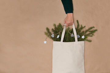 the female hand holds Cotton bag with pine branches and Christmas decor on a craft background. Zero waste. eco friendly Christmas.