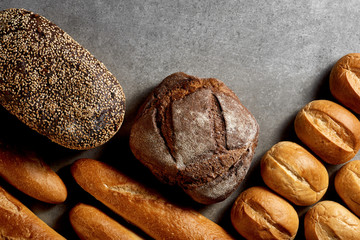 Fresh pastries. Loaves of rye bread, buns and french baguettes on a gray stone surface. Top view.