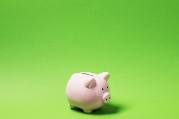 Pink piggy bank on green paper background with copy space