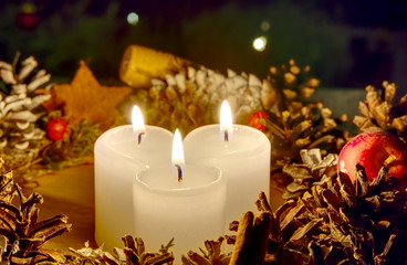 three burning candles with Christmas decoration from pine cones around