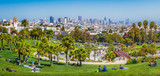 Fototapeta  - Panoramic view of local people enjoying the sunny summer weather at Mission Dolores Park on a beautiful day with clear blue sky with the skyline of San Francisco in the background, California, USA