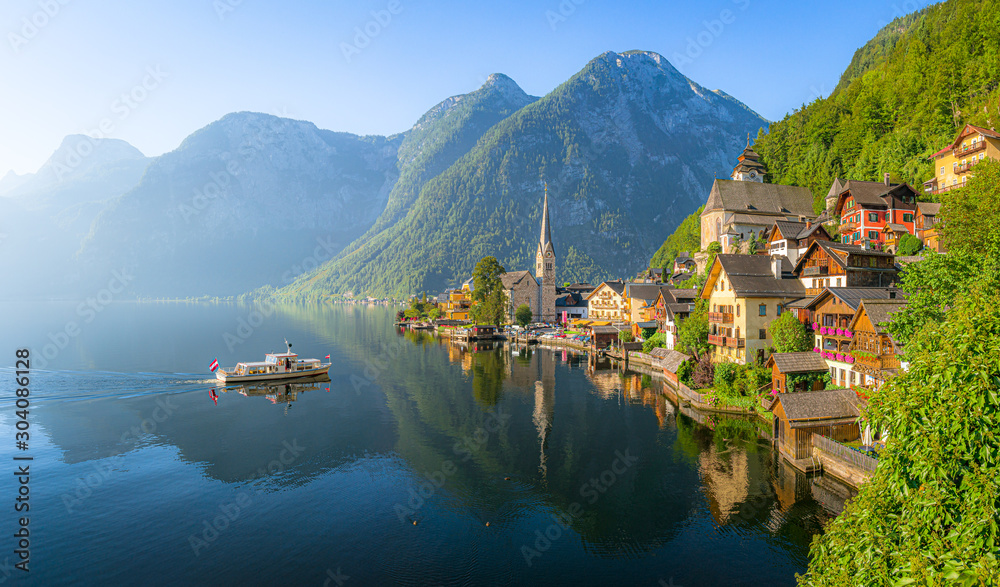 Classic panoramic view of famous old town Hallstatt and alpine deep blue lake with tourist ship in scenic golden morning light on a beautiful sunny day at sunrise in summer, Salzkammergut, Austria - obrazy, fototapety, plakaty 