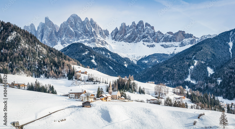 Classic panoramic view of famous Dolomites mountain peaks with the idyllic village Val di Funes and historic Church of St. Magdalena on a scenic sunny day with blue sky in winter, South Tyrol, Italy - obrazy, fototapety, plakaty 