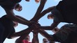 Young athletes stacking their hands together one by one in unity. Group of best friends putting their arms in centre of a circle and raising them up to the blue sky. Friendship and teamwork concept