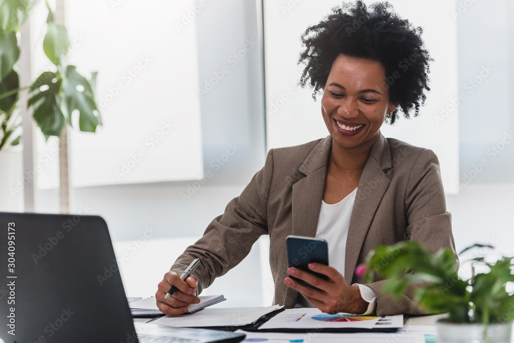 Happy smiling african-american business woman working on laptop at office. Businesswoman sitting at her working place