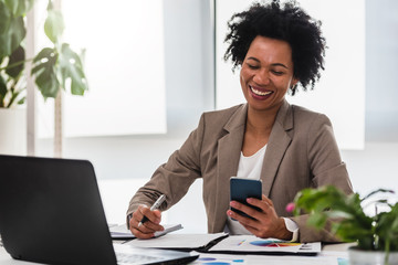 Wall Mural - Happy smiling african-american business woman working on laptop at office. Businesswoman sitting at her working place