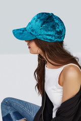 Wall Mural - Cropped side photo of a girl, wearing blue velvet baseball cap with letter P print, white tank top, black jacket and jeans with scuffs. Girl has large hoop earrings. She is posing on a grey background