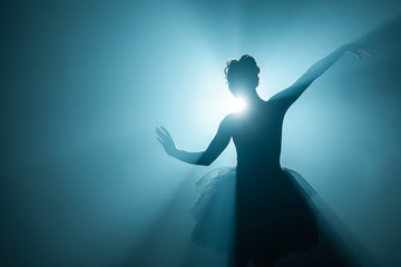 Ballerina in black tutu dress dancing on stage with magic blue light and smoke. Silhouette of young attractive dancer in ballet shoes pointe performing in dark. Copy space.