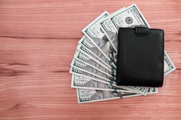 dollars and black wallet on a wooden background.