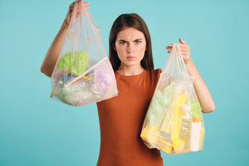 Angry girl in t-shirt holding eco bags with plastic waste wrathfully looking in camera over colorful background