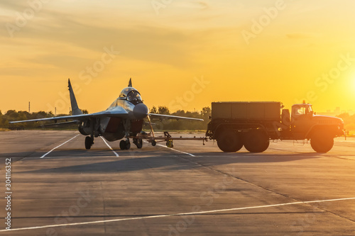 Tela Military fighter is being pushed to a parking lot by a military vehicle at an air base in the evening at sunset