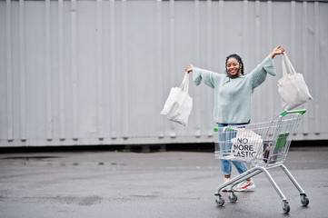 Wall Mural - No more plastic. African woman with shopping cart trolley and eco bags posed outdoor market.