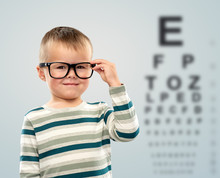 School, Education And Vision Concept - Portrait Of Smiling Little Boy In Glasses Over Eye Test Chart Background