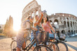 Three happy young women friends tourists with bikes taking selfies at Colosseum in Rome, Italy at sunrise.