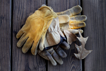 Old leather work gloves with leaf on wooden background