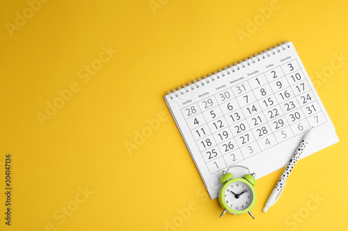 Fotografía Calendar, pen and alarm clock on yellow background, flat lay