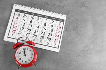 Calendar and alarm clock on grey stone background, above view