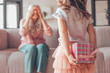 © Afshar Tetyana - girl holding present box in the hands behind her back and making surprise for grandmother sitting on the couch