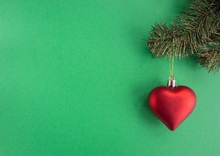 Christmas New Year Composition With Heart Red Ball  And Xmas Tree On Green Background. Greeting Card. Flat Lay, Top View, Copy Space.