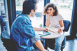 © BullRun - Meeting of two friends at coffee table in cafeteria.Positive casual dressed young woman communicating with hipster guy dressed in casual wear about common design project.Cooperation of two students