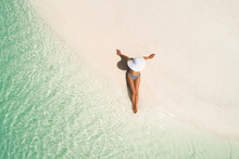 Summer Holiday Fashion Concept - Tanning Girl Wearing Sun Hat At The Beach On A White Sand Shot From Above.Top View From Drone. Aerial View Of Slim Woman Sunbathing Lying On A Beach In Maldives.