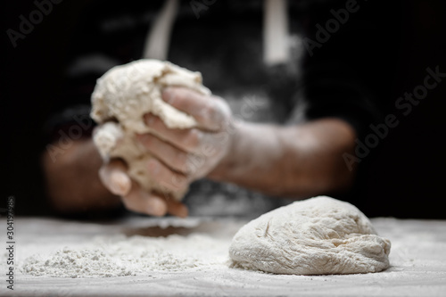 Cuadros en Lienzo Hands of male baker preparing yeast dough with white flour dust on black backgro