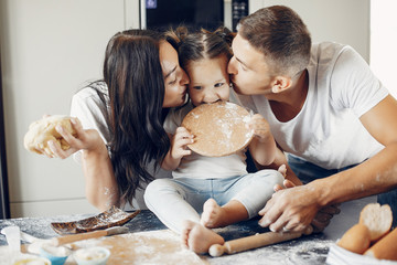 Family in a kitchen. Little girl with a dough. Mother and father in a white t-shirts